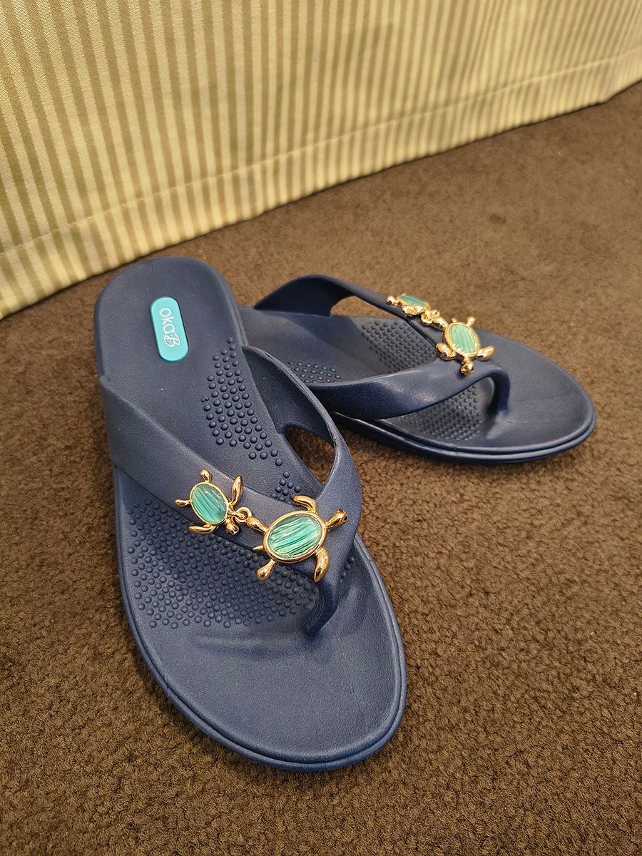 Blue flip-flops with gold turtle embellishments on a brown carpet.