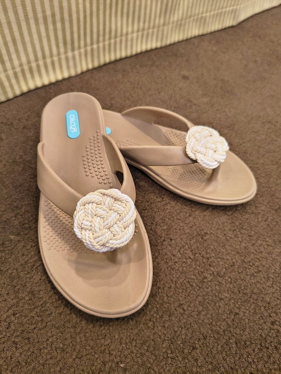 Beige flip-flops with woven white flower embellishments on a brown carpet