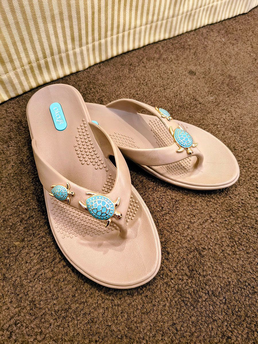 Beige beaded thong sandals on a carpeted floor near a striped sofa edge