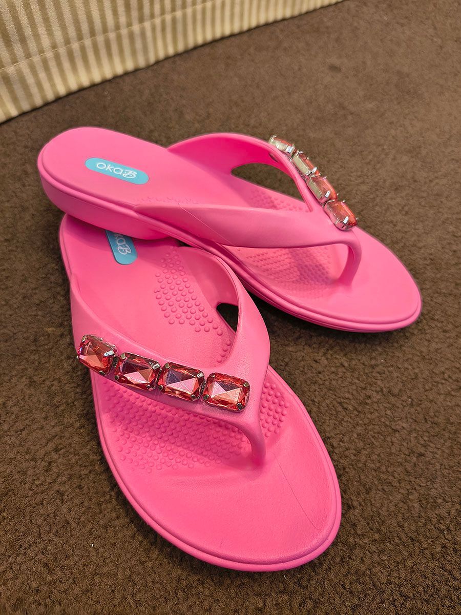 Pink jeweled flip-flops on a brown carpeted floor