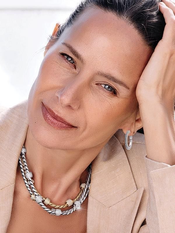 A woman wearing a necklace and hoop earrings is smiling.