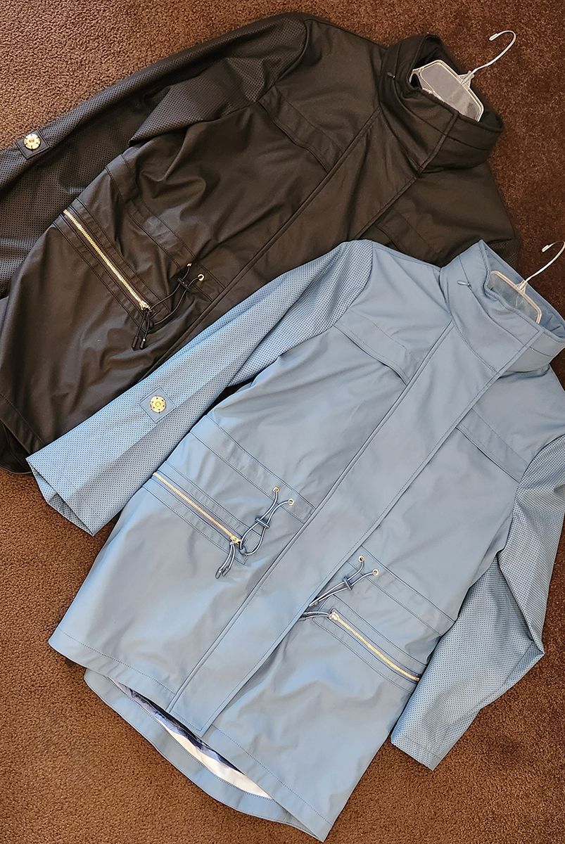 Two jackets laid out on a textured surface: one black and one light blue, both with zippers.