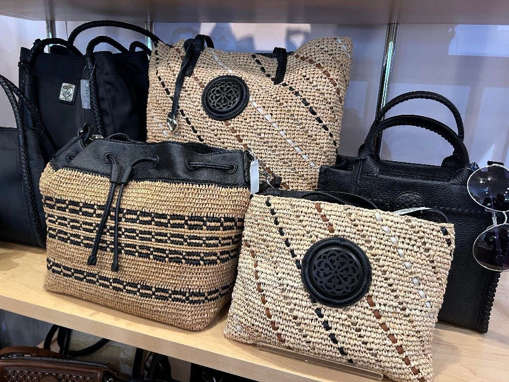 Assorted woven handbags in black, beige, and tan displayed on shelves.