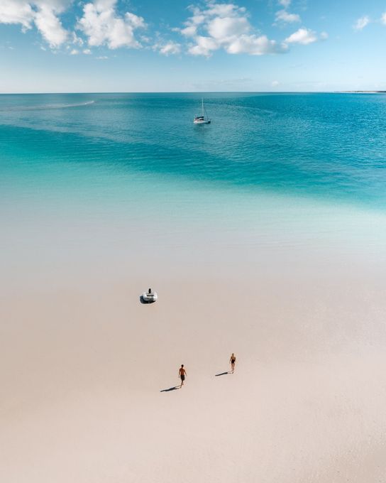 Aerial view of visitors walking across a pristine white sand beach beside turquoise tropical waters