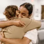 Two women are hugging each other in a room.