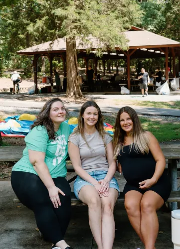 Three women are sitting on a picnic table in a park.
