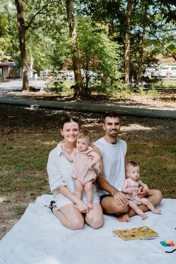 A family is sitting on a blanket in a park.