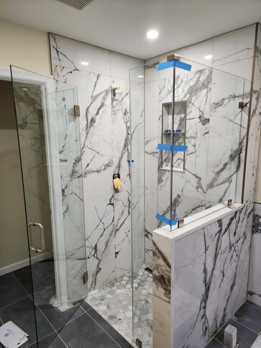 Marble-tiled shower with clear glass doors and gold hardware.