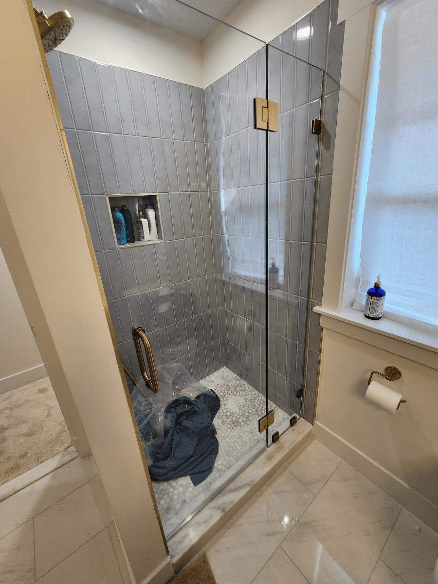Shower stall with gray textured tile, clear glass door, and gold hardware.