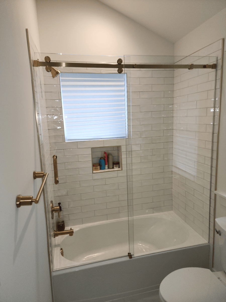 Bathroom with white subway tile, a bathtub, and a glass shower door with gold hardware.