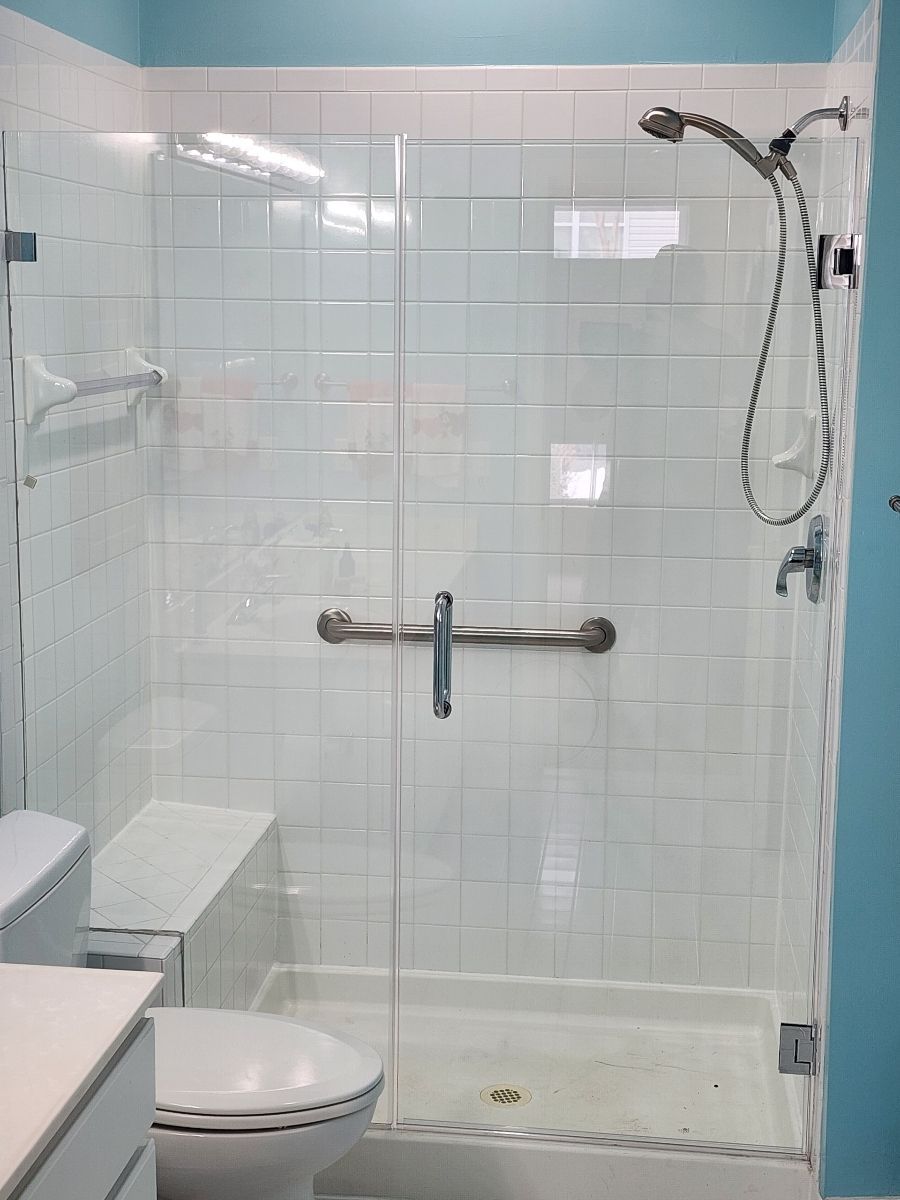 Glass shower enclosure with white tile walls, grab bar, and handheld showerhead.