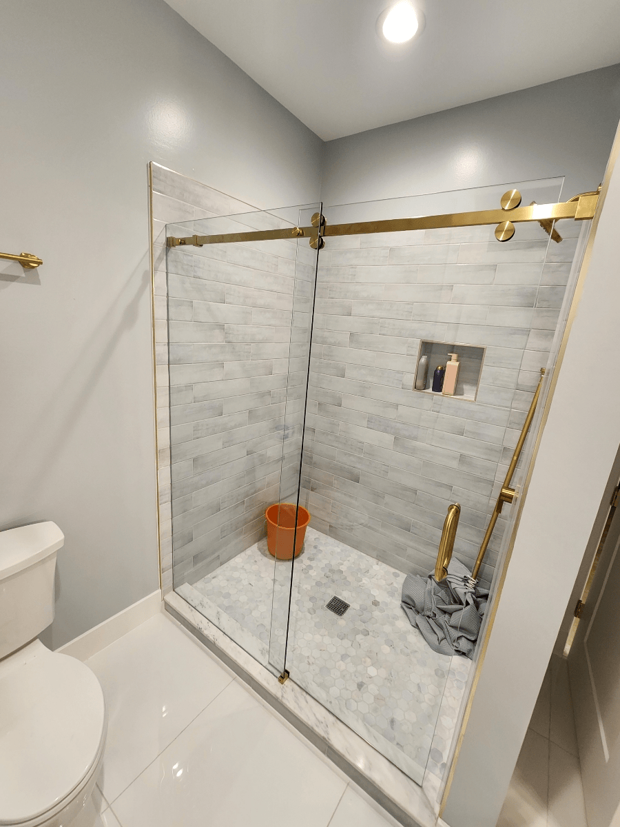 Bathroom with glass shower, gold fixtures, marble tile, gray walls, and white toilet.