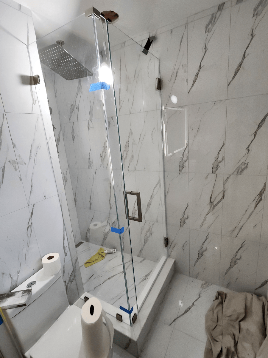 Glass shower enclosure in a marble-tiled bathroom. A rain showerhead is mounted on the wall.