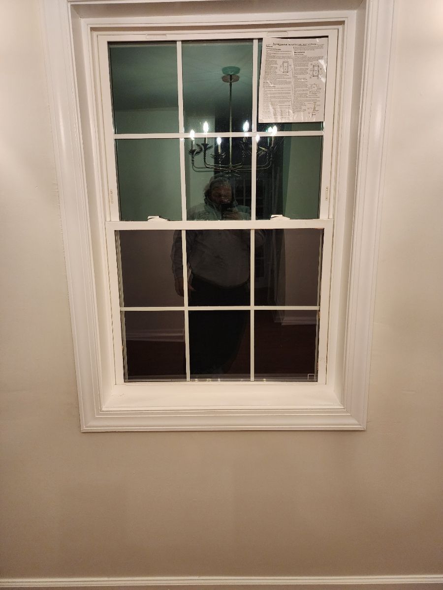 White framed window on a beige wall reflecting a room with a chandelier.