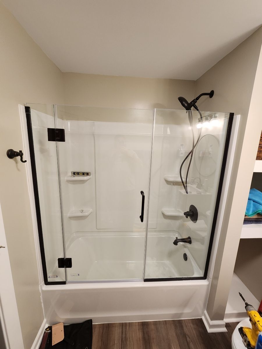 Bathroom with white tub, clear glass shower doors, black fixtures, and light brown walls.