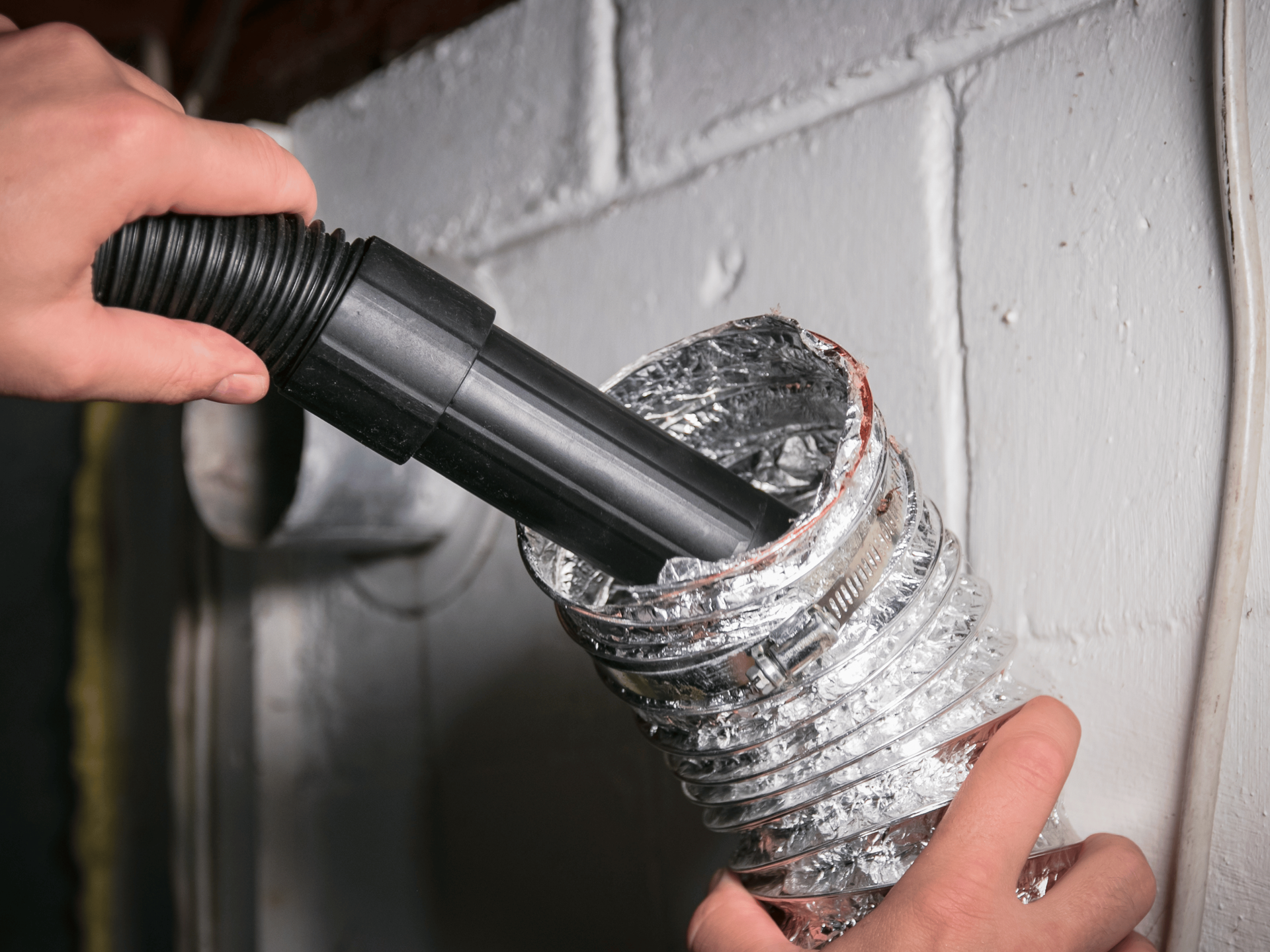 Person vacuuming a dryer vent with a vacuum hose.