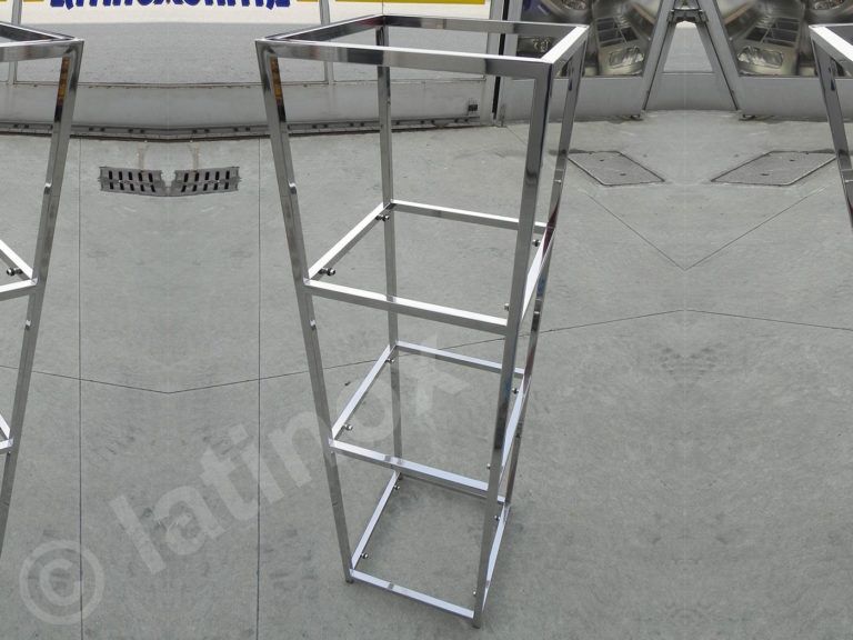 Espositore in metallo argentato su una superficie in cemento grigio, con una struttura a forma di scatola e tre ripiani.