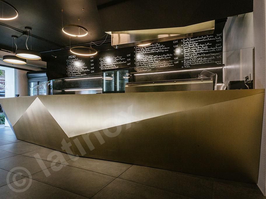 Un moderno bancone da ristorante con design geometrico e luci calde. Sullo sfondo si vedono i menù.