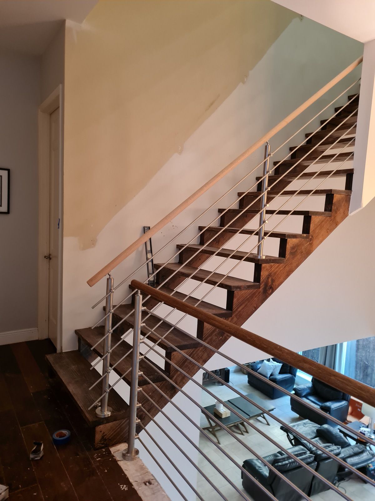A wooden staircase with cable railings leads from a residential landing to an open living area below.