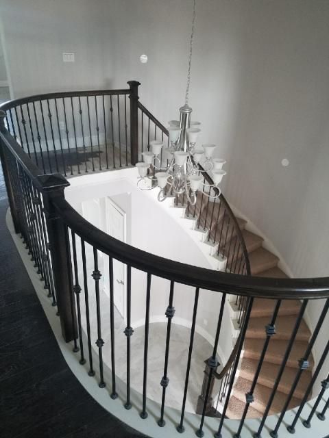 A curved staircase with dark wooden railings and iron balusters, featuring a chandelier hanging in the open foyer above.