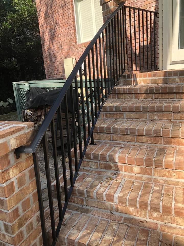 Black metal handrail running alongside outdoor brick stairs leading to a doorway.