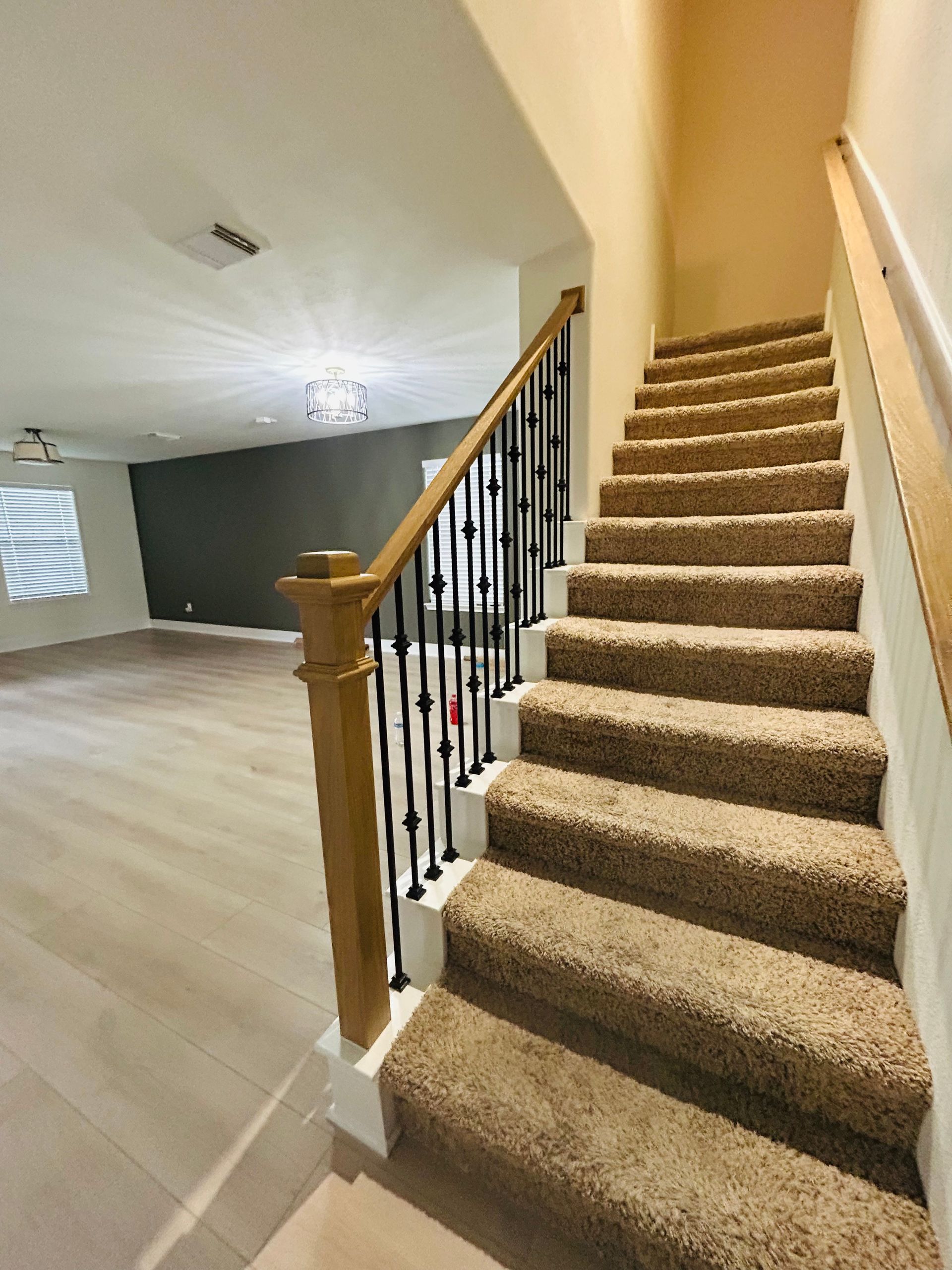 Carpeted staircase with wooden banister and black balusters in a bright, empty interior room