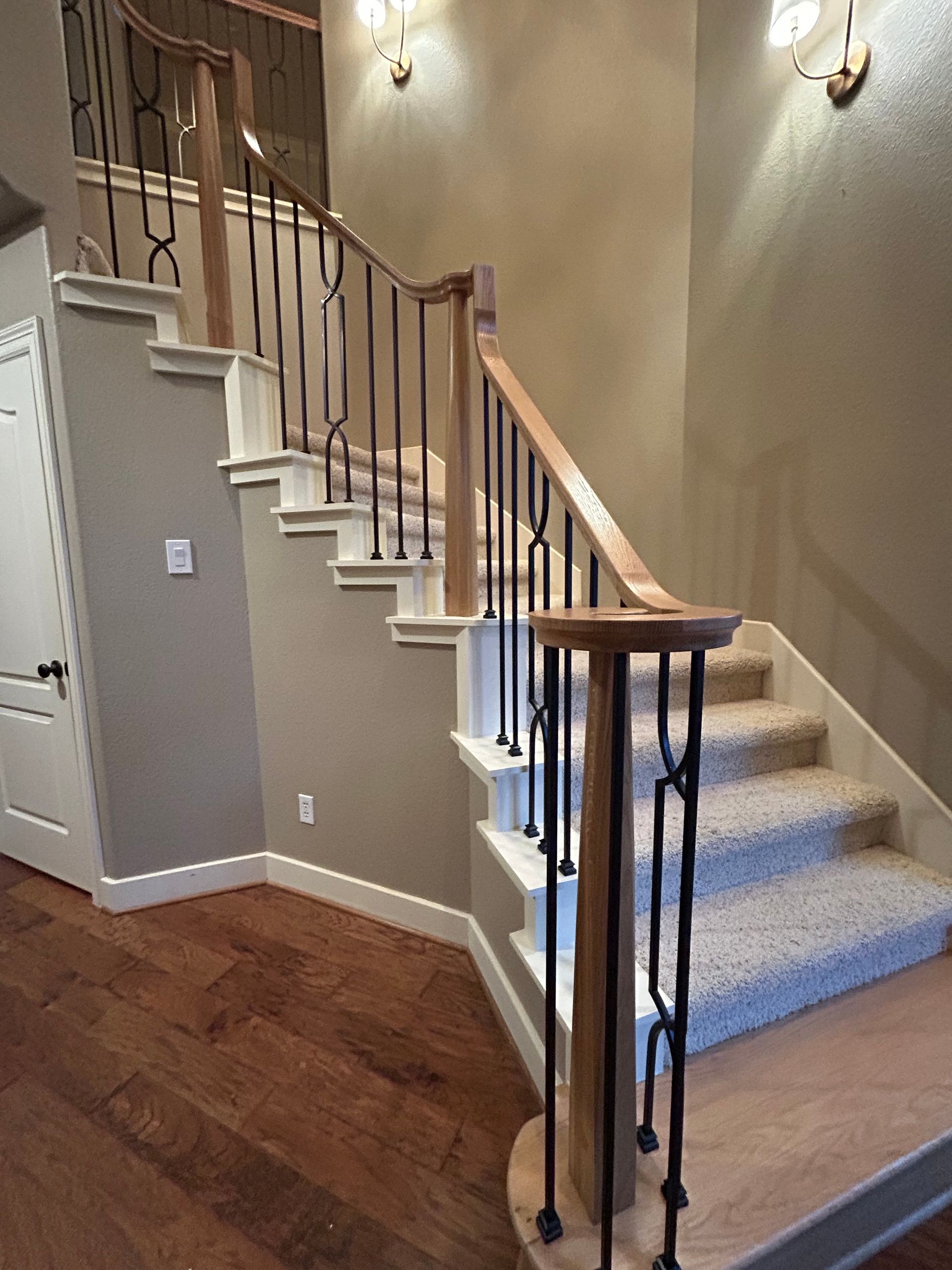 Indoor staircase with curved wooden banister, beige walls, and carpeted steps leading upstairs