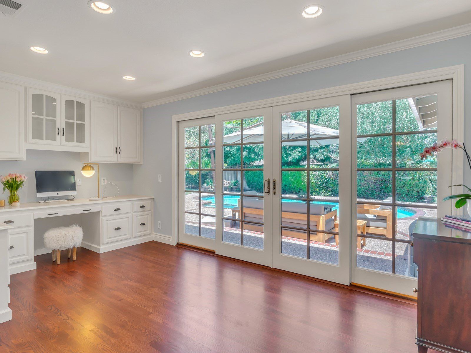 Room with desk, cabinets, and glass doors opening to a backyard pool area.