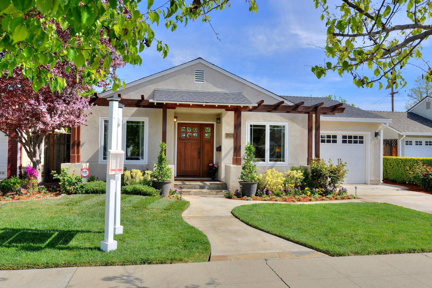 Tan bungalow with brown trim, wooden front door, and green lawn.