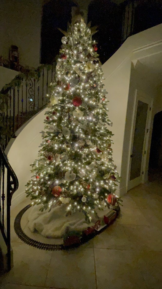 Lit Christmas tree with ornaments, lights, and a train set on a circular base.