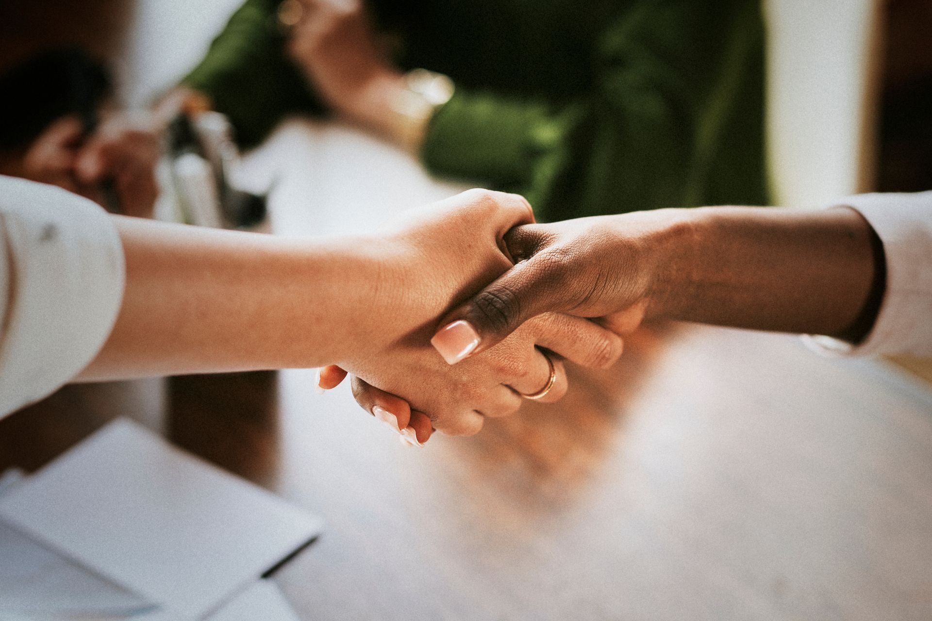 Two people shaking hands over a table; one person is light-skinned, the other is dark-skinned.