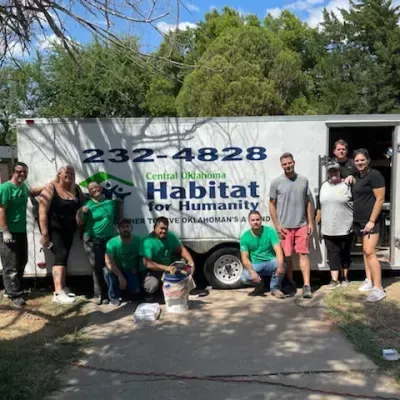 Group of volunteers in green shirts posing in front of a Habitat for Humanity trailer.
