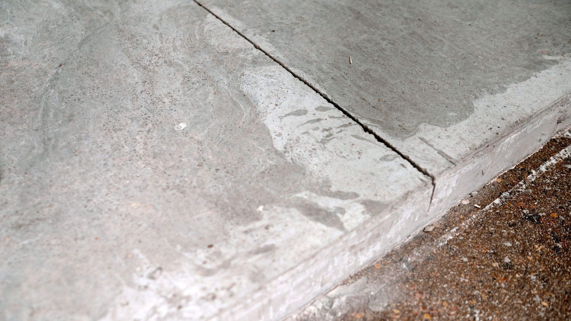 Concrete sidewalk corner with a visible crack and white patching beside gravel