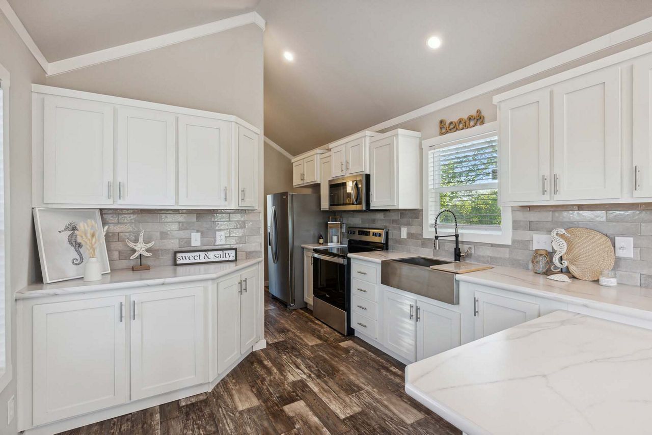 Modern white kitchen with black countertop, stainless steel stove, and fruit bowl by the window