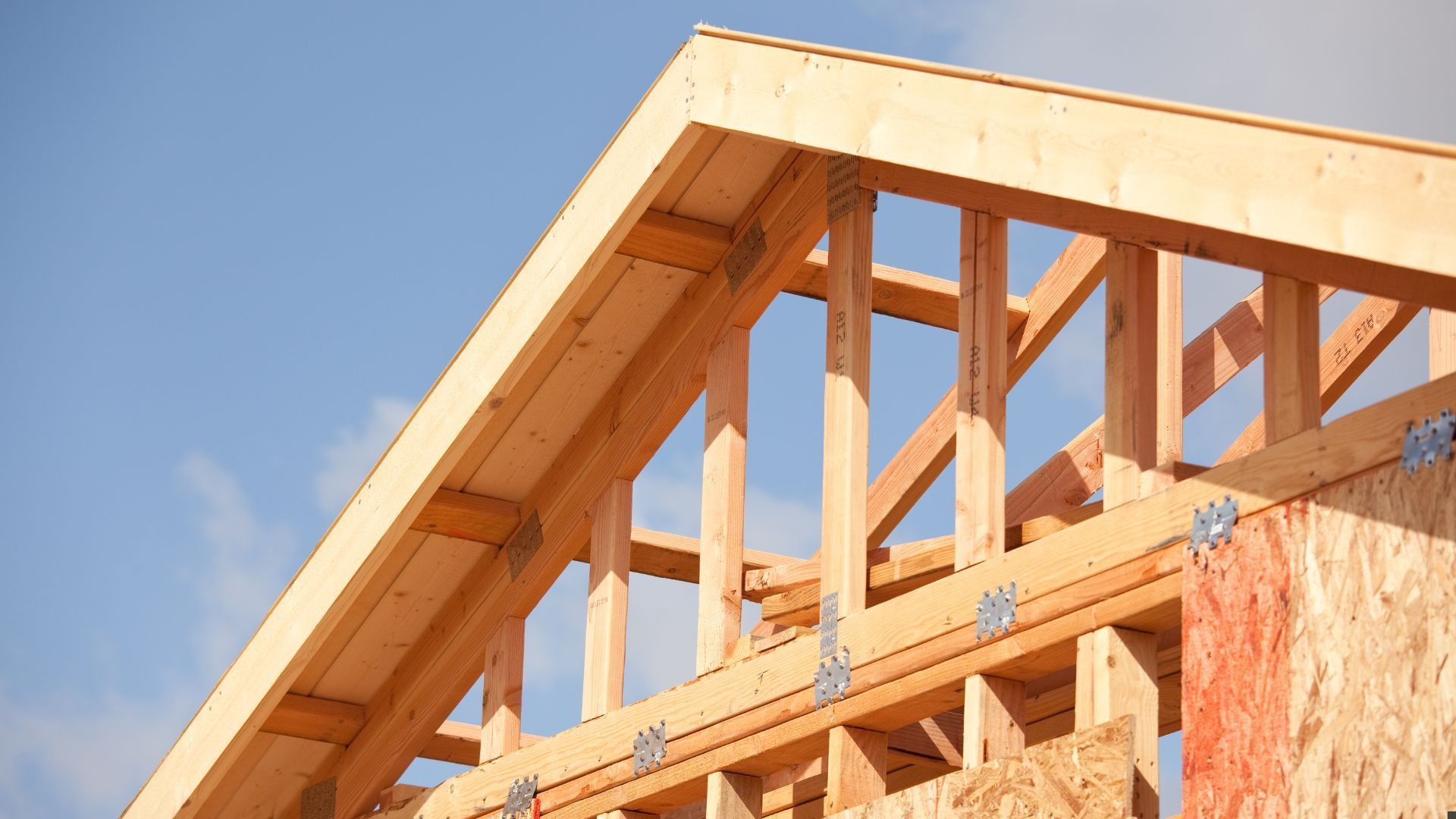 Wooden house frame under construction against a blue sky
