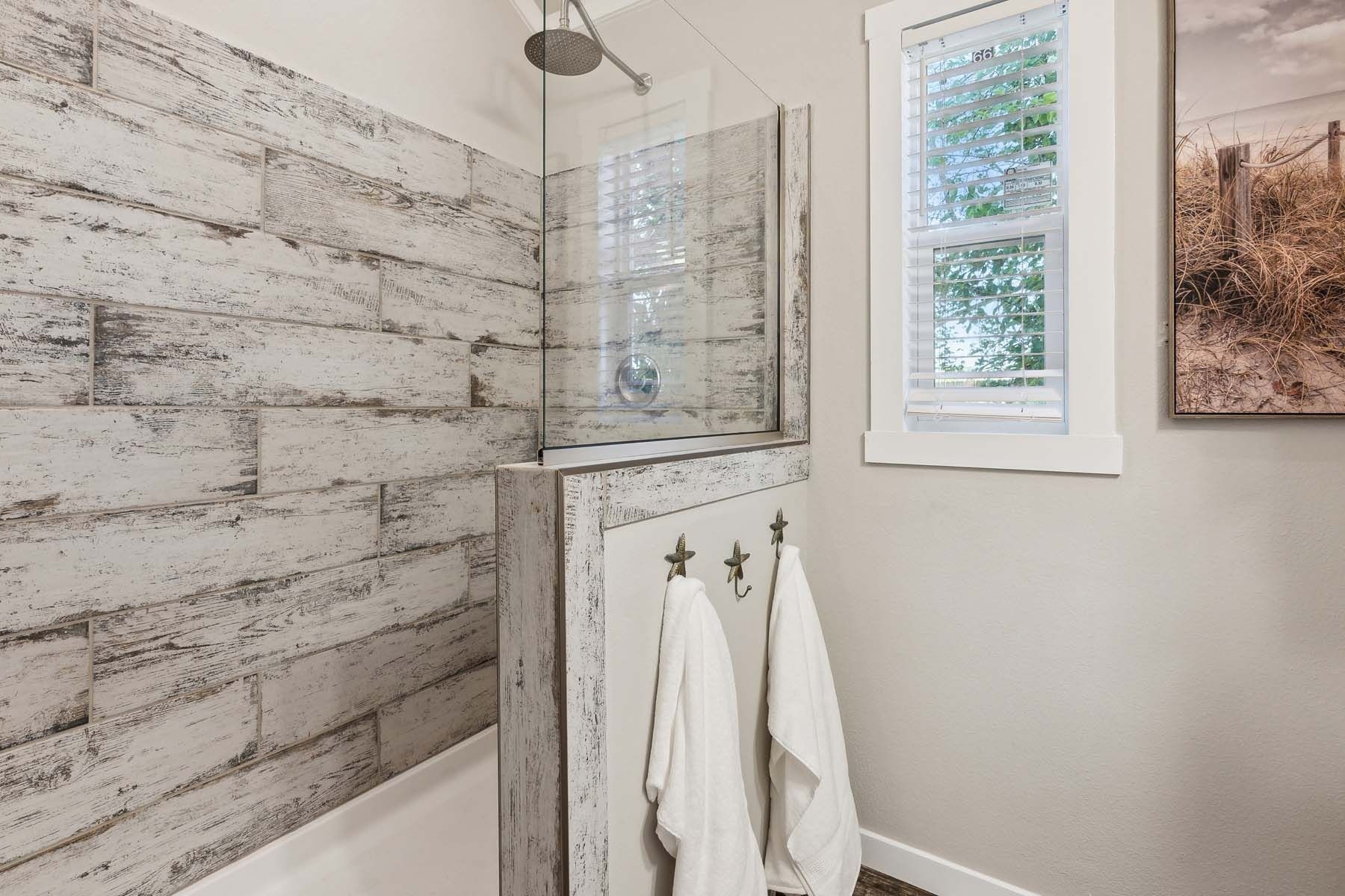 Bright bathroom shower with whitewashed wood-look wall, small window, towel rack, and hanging white robes