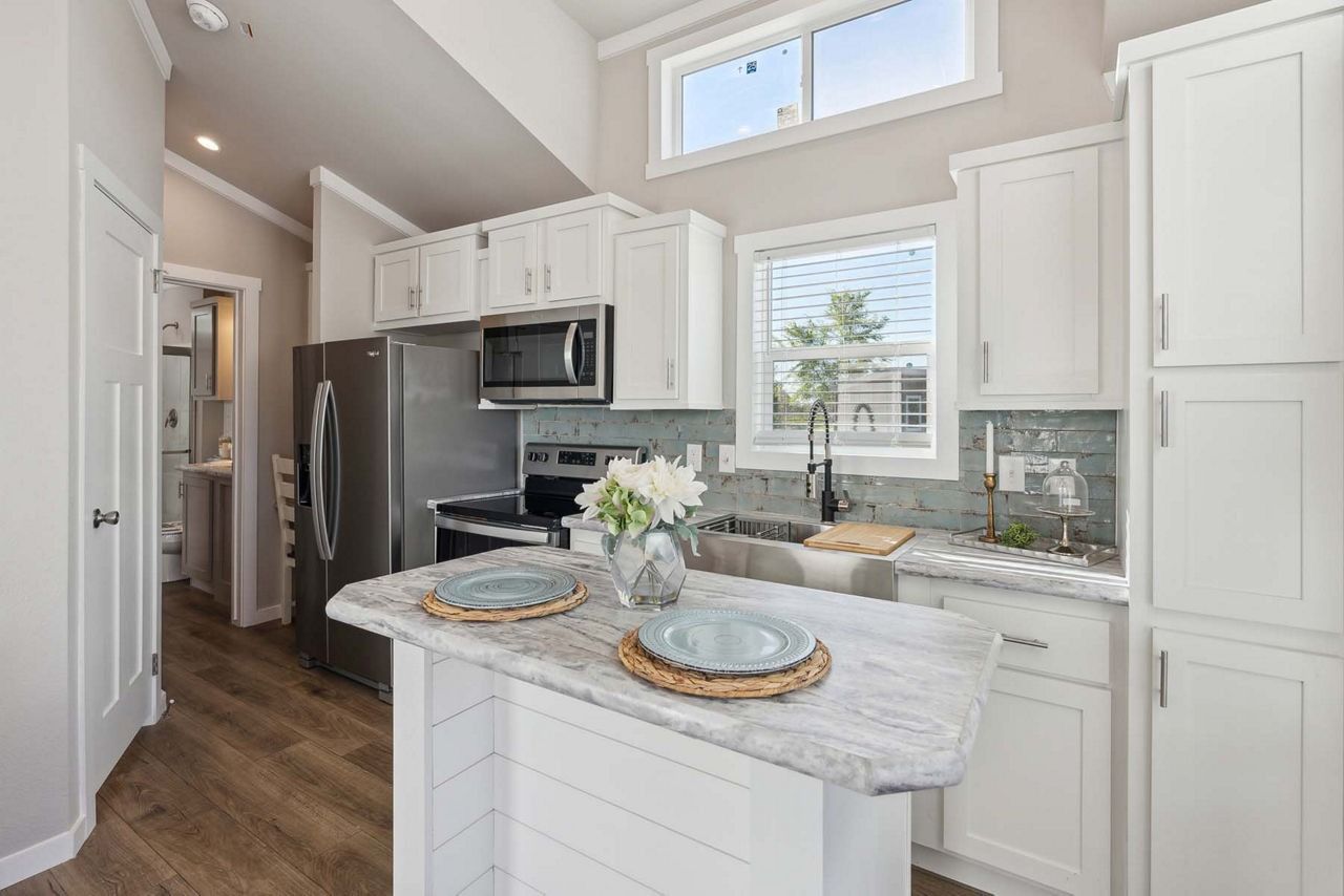 Bright white kitchen with island, stainless appliances, and a window above the sink