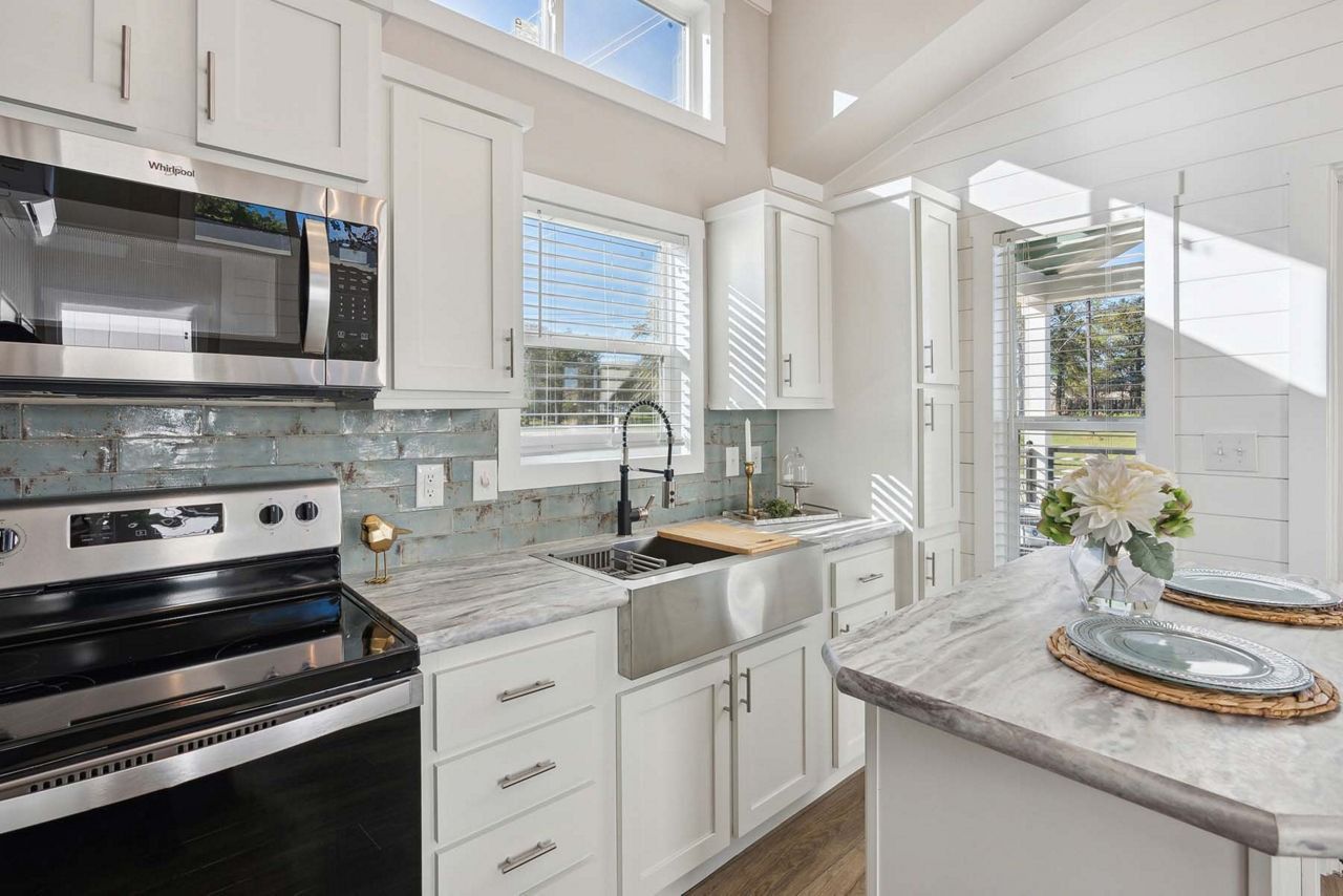 Bright white kitchen with stainless steel stove, farmhouse sink, and granite island in sunlight