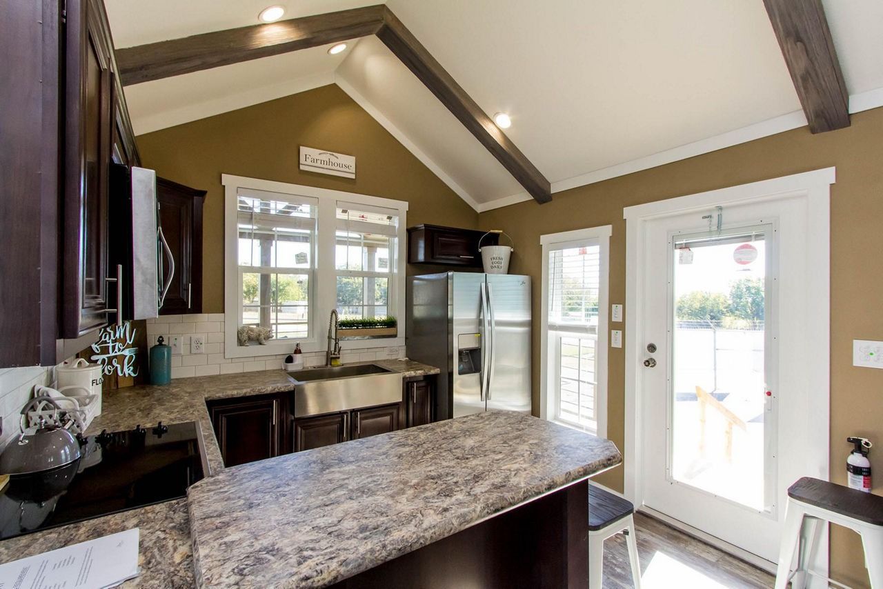 Bright kitchen with granite island, dark cabinets, vaulted ceiling, and white back door.