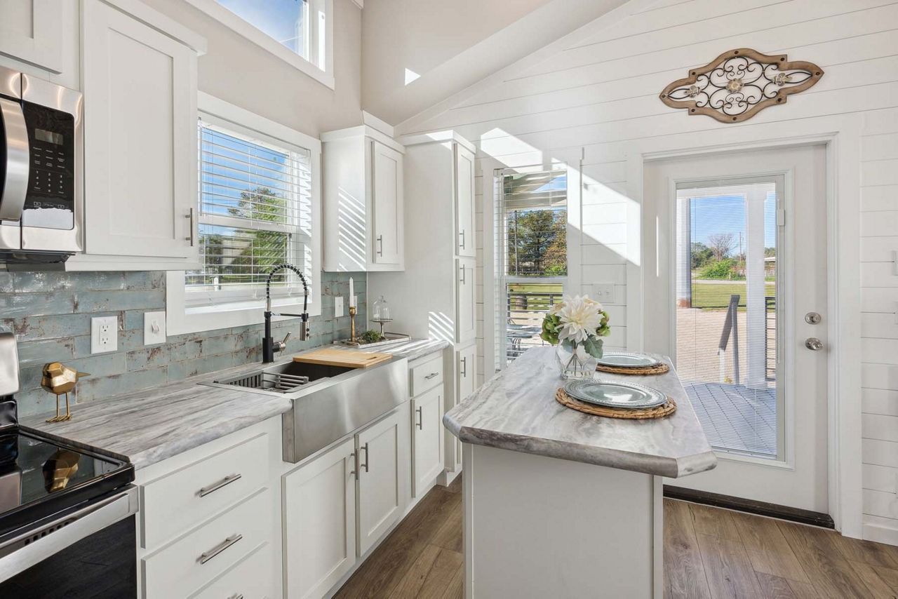 Bright white kitchen with granite island, stainless appliances, and open door to backyard under vaulted ceilings