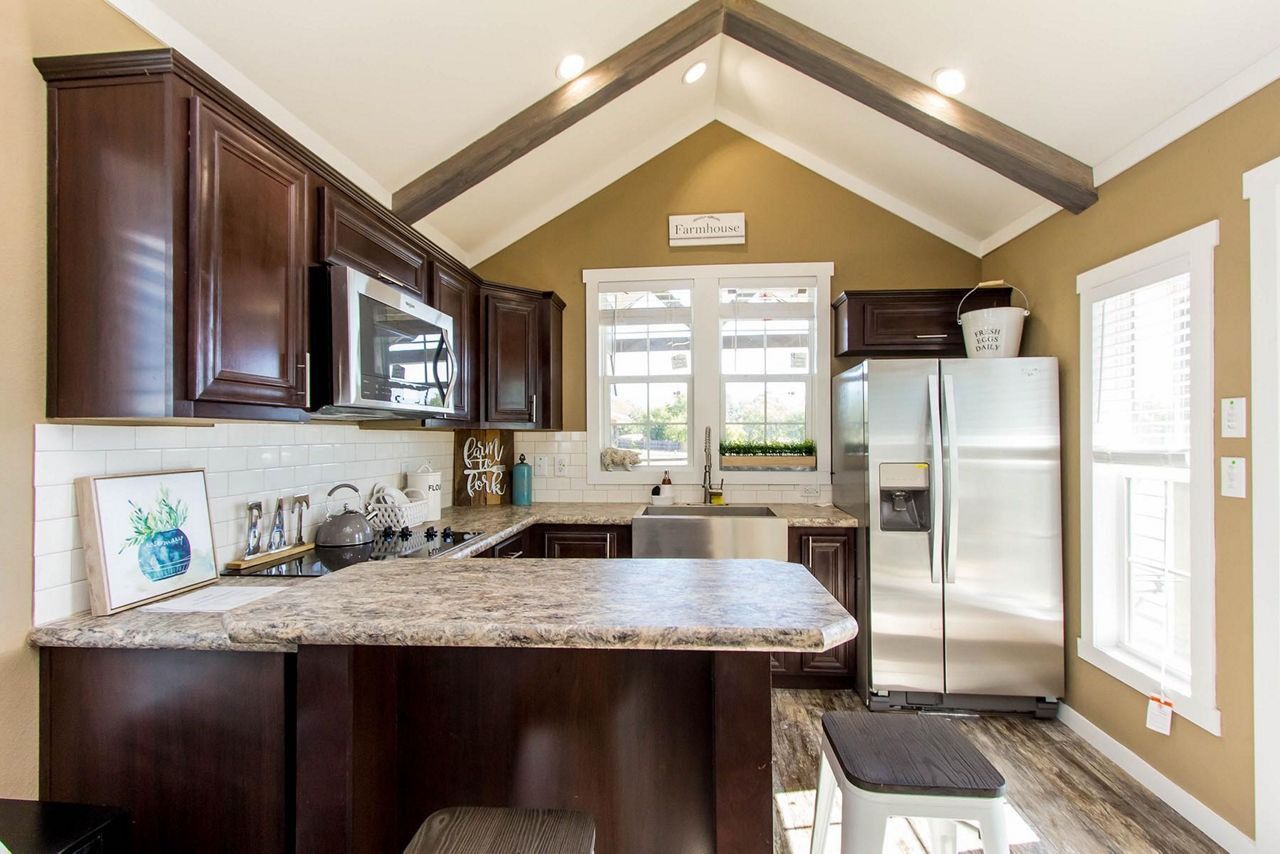 Modern kitchen with dark wood cabinets, granite counters, stainless fridge, and vaulted ceiling.