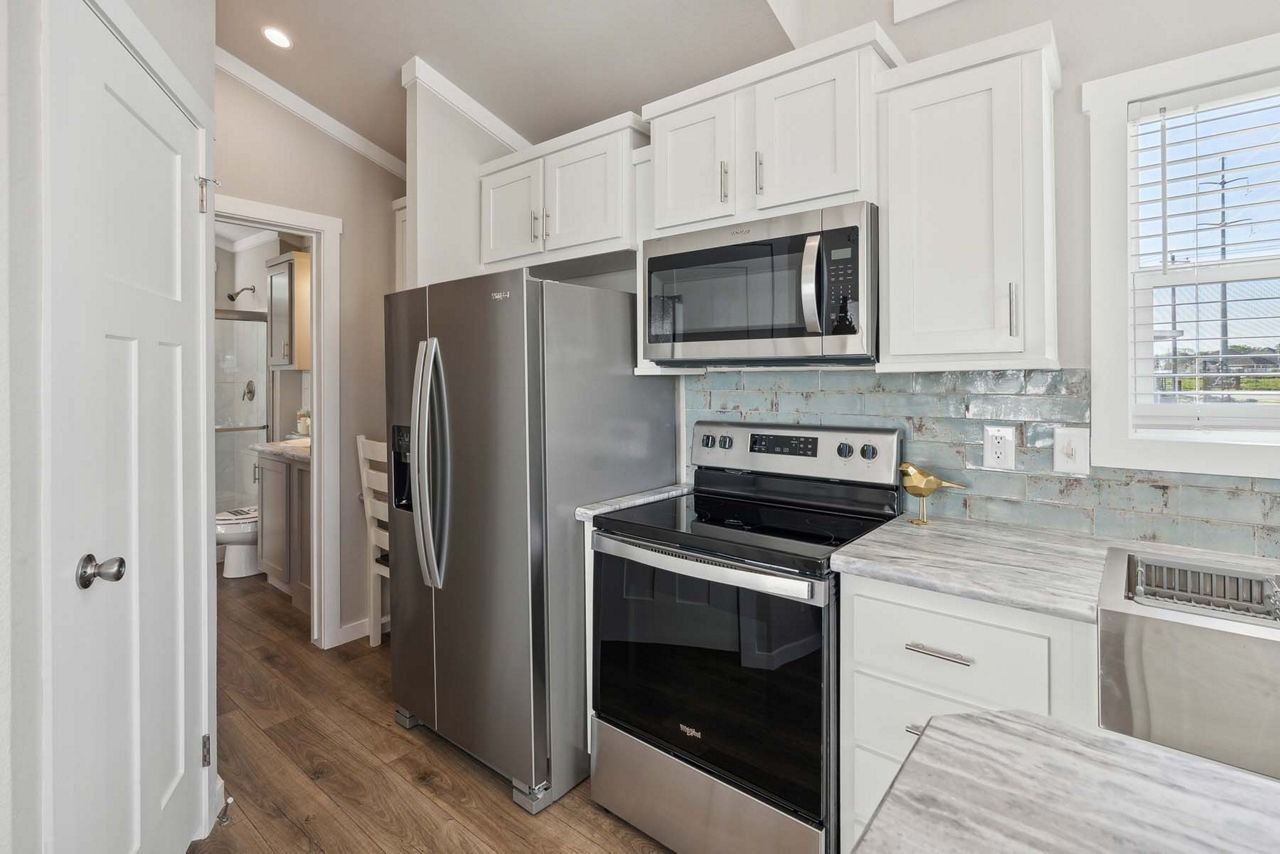 Bright white kitchen with stainless steel appliances, light wood floors, and a window over the counter.