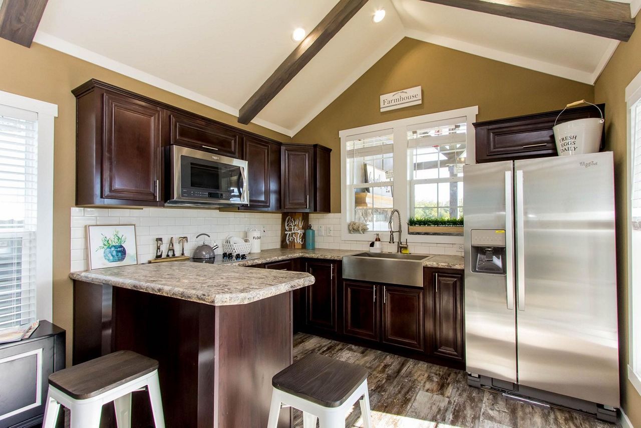 Modern kitchen with dark wood cabinets, granite island, stainless fridge, and window above the sink