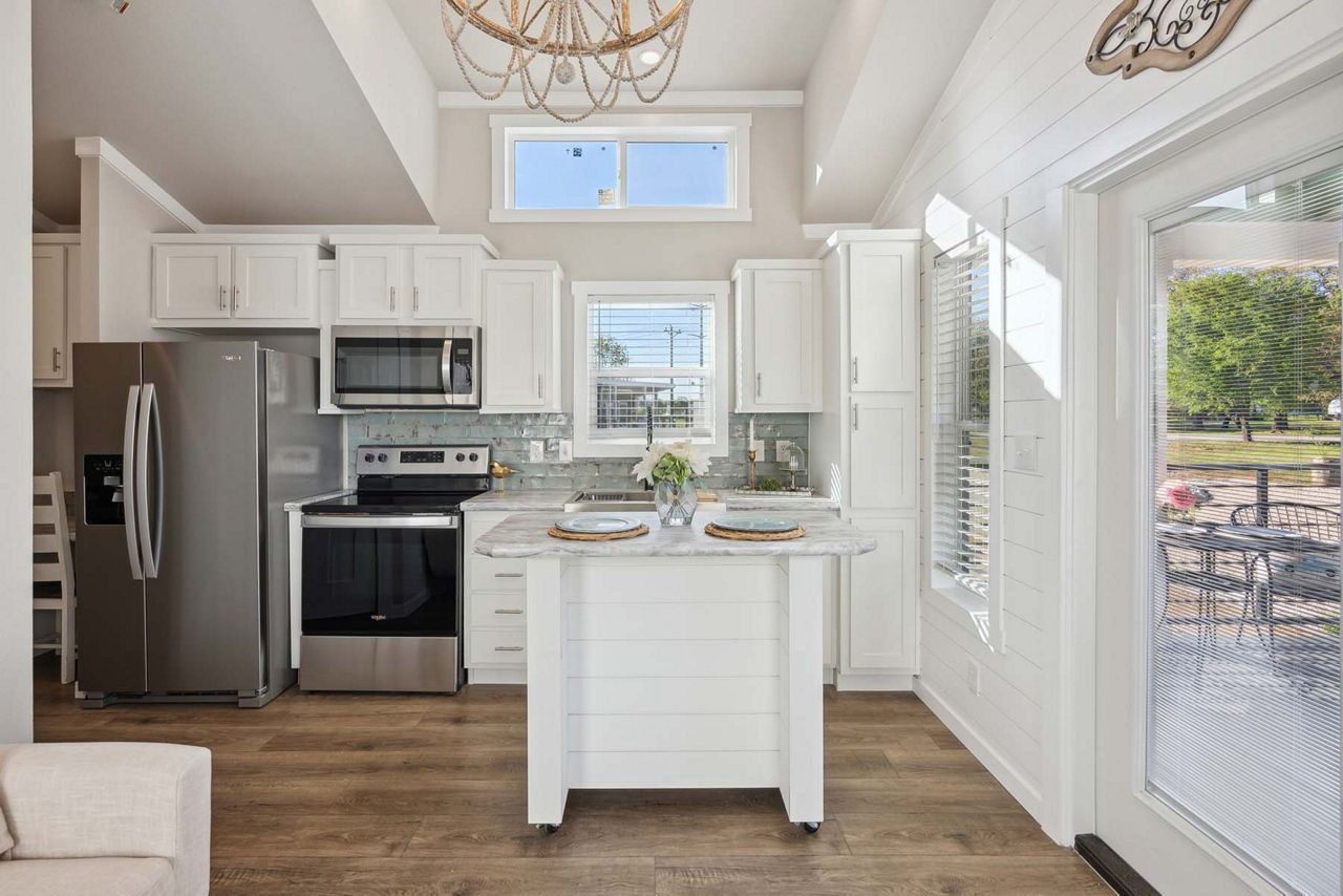 Bright white kitchen with stainless appliances, island, wood floors, and a glass door to the patio.
