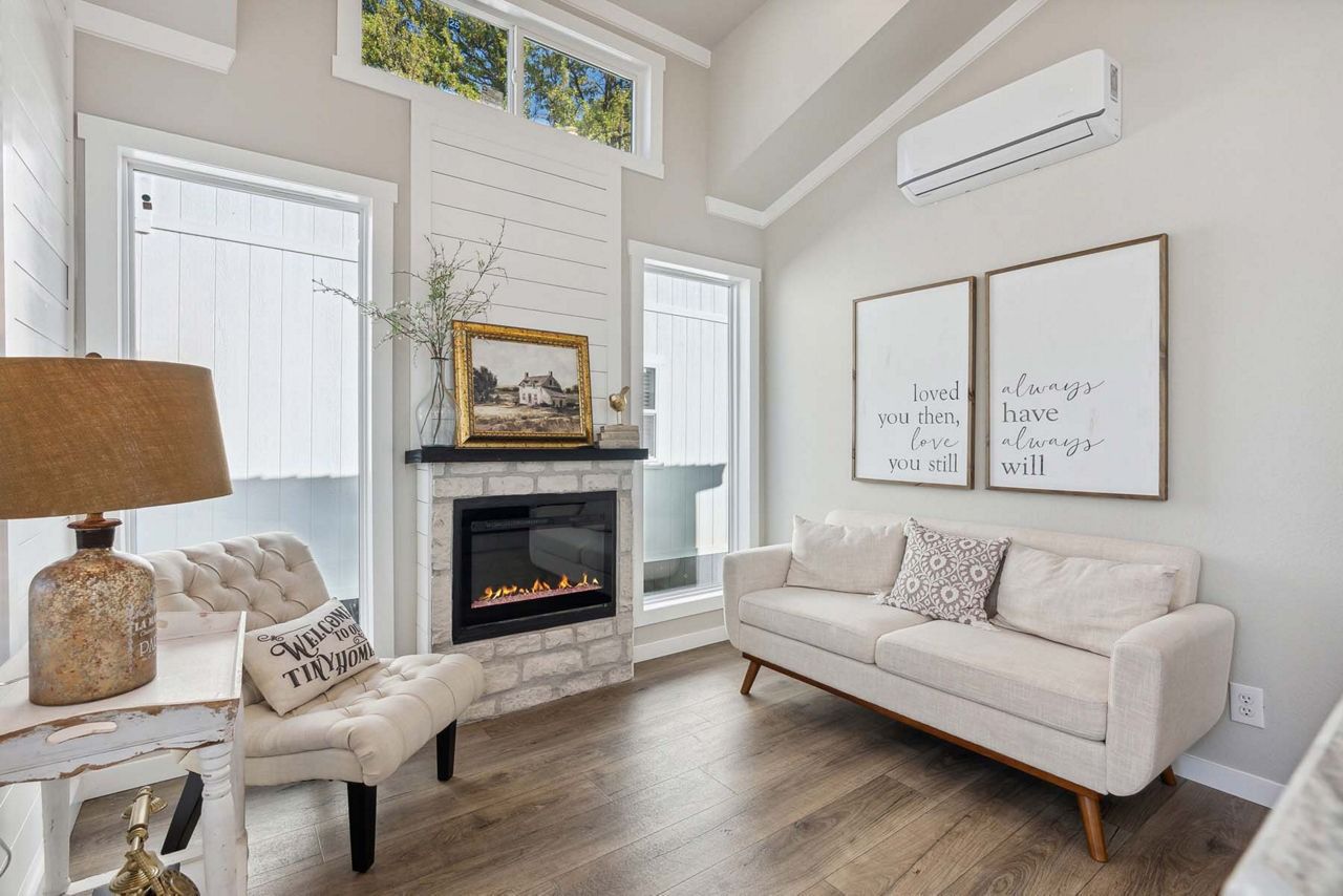 Bright living room with white sofa, fireplace, and wall art, with natural light and a woven lamp.