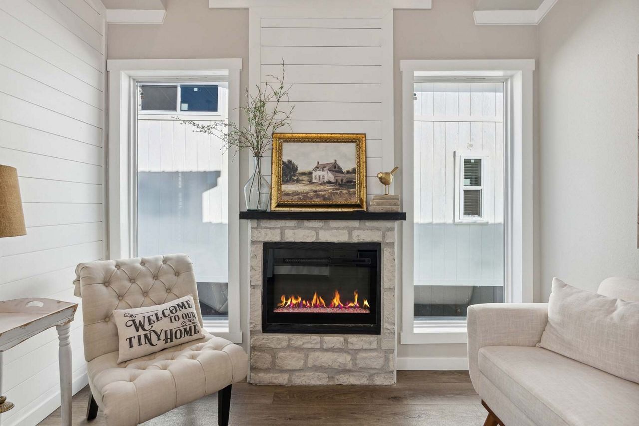 Bright living room with fireplace, tufted chairs, beige sofa, and a framed painting on the mantel