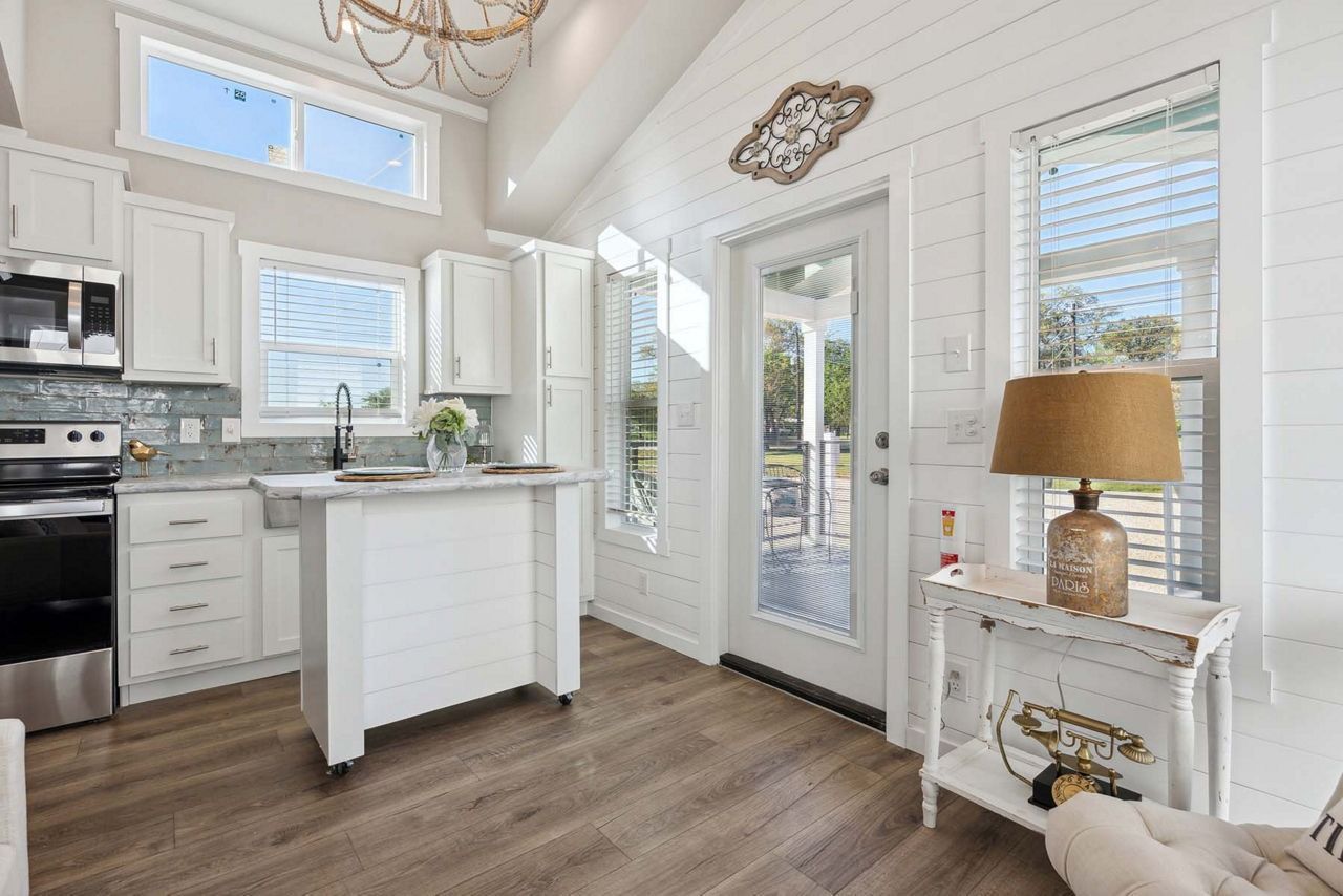 Bright white kitchen with island, stainless appliances, wood floors, and glass door to a porch
