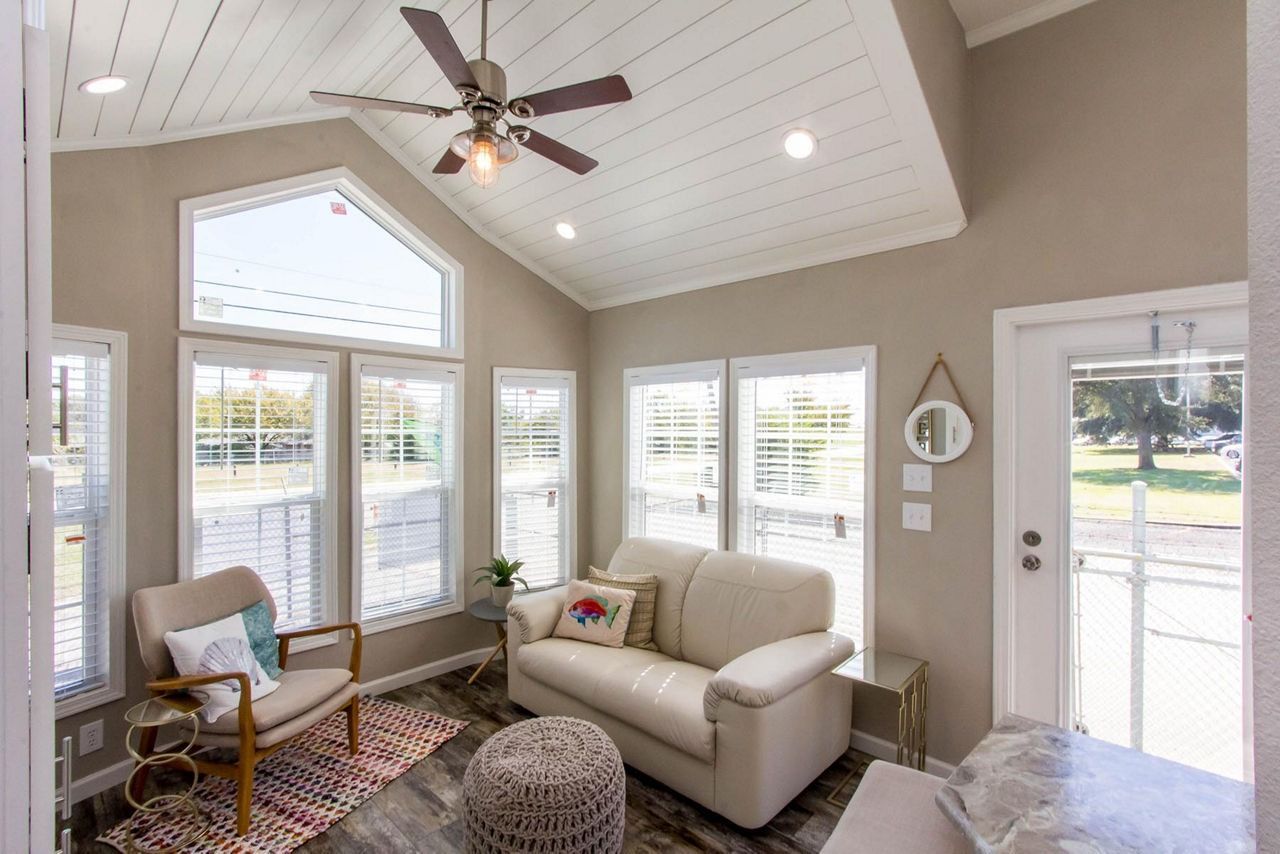 Bright sunroom with white sofa, woven chair, bay windows, ceiling fan, and glass doors to the yard.