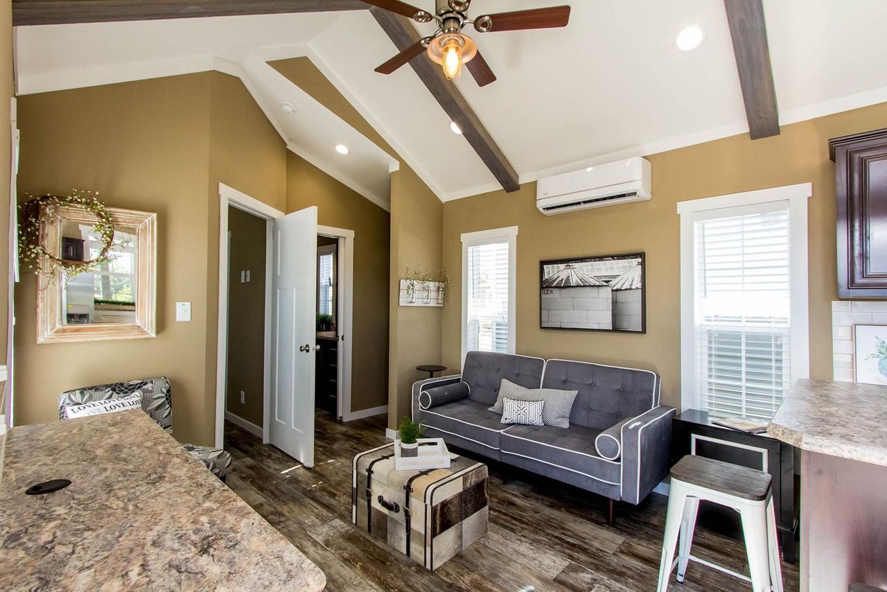 Modern living room with gray sofa, granite bar, ceiling fan, vaulted ceiling, and wall-mounted air conditioner
