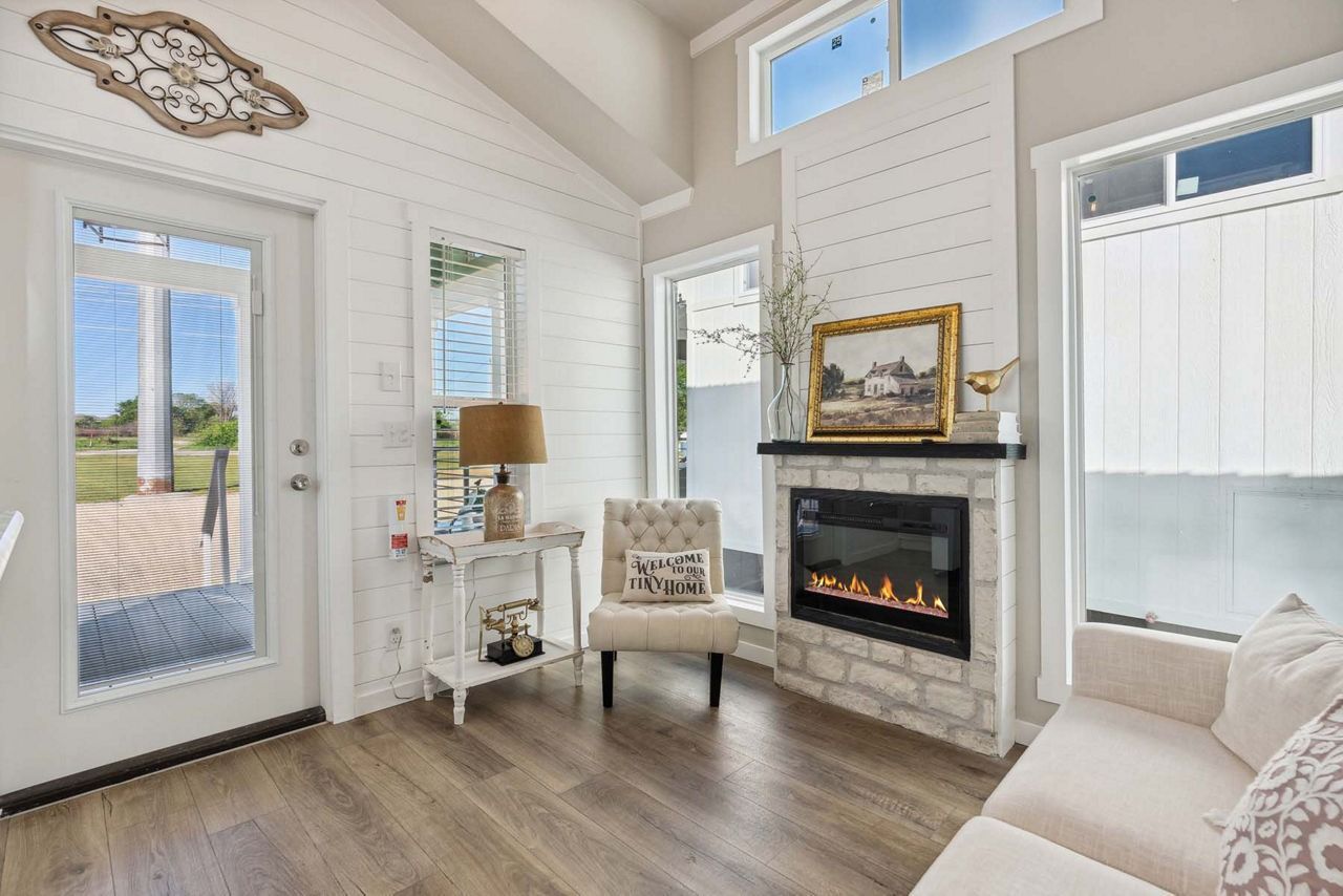 Bright living room with fireplace, high windows, glass door, white walls, and light wood floors